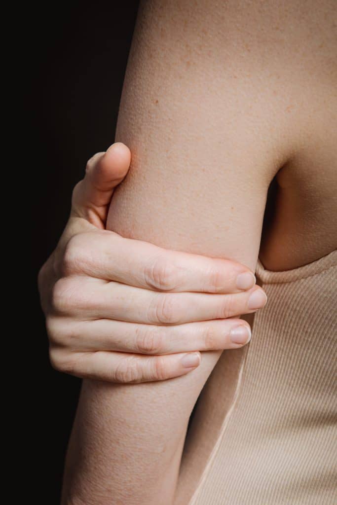 A woman touching her pale arm with her pale hands.